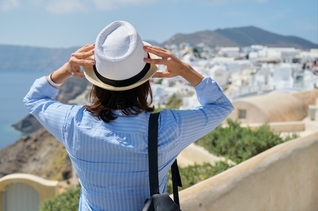 Mulher feliz turista com chapéu e mochila olhando a paisagem da ilha de Santorini