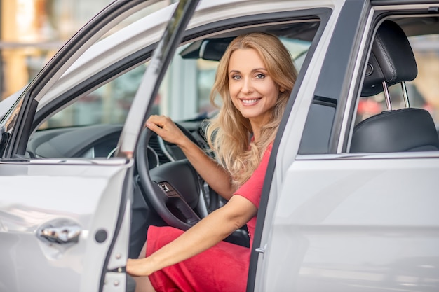 Mulher feliz. Uma linda mulher com um vestido vermelho sentada em um carro vermelho e parecendo feliz