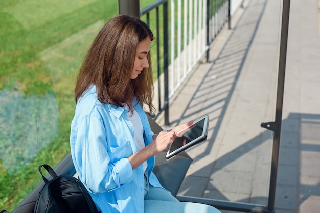 Mulher feliz usa um tablet ou ebook em uma estação de bonde enquanto aguarda o transporte público.