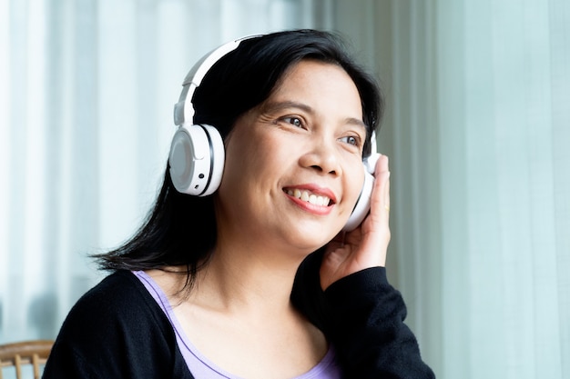 Mulher feliz usando fone de ouvido sem fio sobre a orelha branco ouvindo música em casa