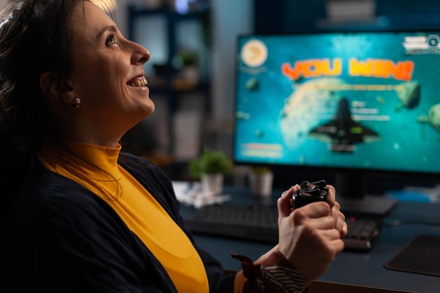 Mulher feliz usando joystick para jogar videogame no computador. gamer ganhando jogos online com controlador na frente do monitor. pessoa se sentindo alegre e comemorando a vitória na internet.
