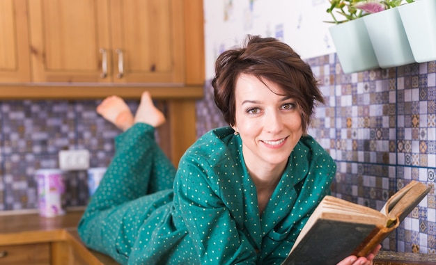 Mulher feliz usando pijama e relaxando em casa lendo um livro