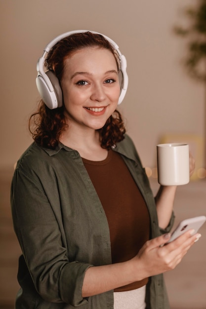 Mulher feliz usando smartphone e fones de ouvido em casa enquanto toma um café