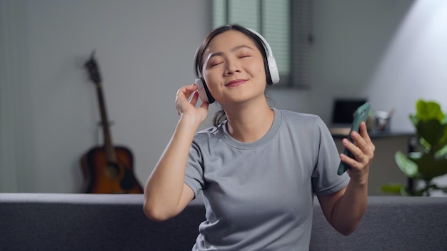 Mulher feliz usando telefone inteligente com fones de ouvido ouvindo música sentado no sofá na sala de estar em casa