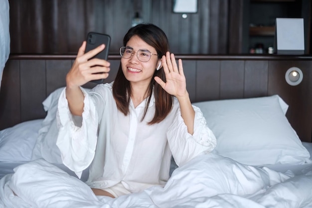 Mulher feliz usando telefone inteligente para reunião feminina de videochamada on-line por telefone celular na rede de tecnologia de cama trabalho em estilo de vida doméstico e conceito de comunicação digital