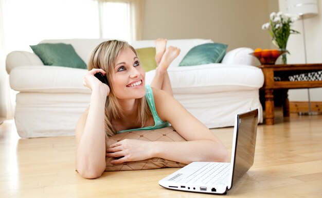 Mulher feliz usando um laptp deitado no chão