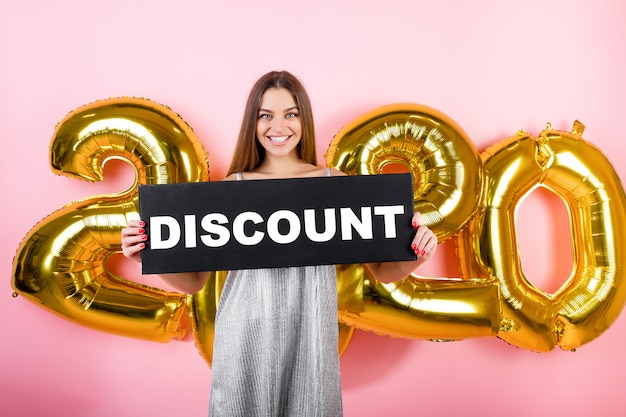 Foto mulher feliz usando vestido com sinal de desconto copyspace com balões 2020 isolados sobre rosa