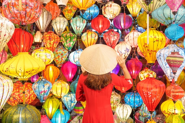Mulher feliz usando vestido vietnamita Ao Dai com lanternas coloridas viajante passeando em Hoi An cidade antiga no centro do Vietnãmarco para atrações turísticasVietnã e conceito de viagem do sudeste