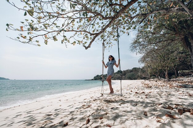 Mulher feliz viajante em vestido estilo pin-up xadrez branco e preto relaxante no balanço. Praia turística do mar Tailândia, Ásia, viagem de viagem de férias de férias de verão. Phuket. Tailândia