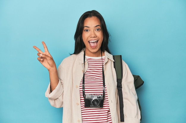 Mulher filipina com câmera e mochila em azul alegre e despreocupada