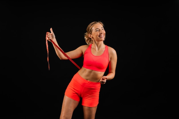Mulher fitness com fita métrica mostrando a cintura em um fundo de estúdio