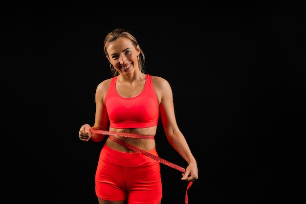 Mulher fitness com fita métrica mostrando sua cintura no fundo do estúdio
