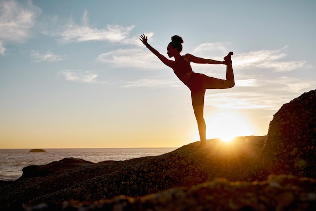 Foto mulher fitness e ioga se alongando na praia durante o pôr do sol para treinamento de bem-estar espiritual ou treino mulher ativa em zen calmo ou alongamento de aquecimento para exercícios saudáveis posando em uma rocha oceânica