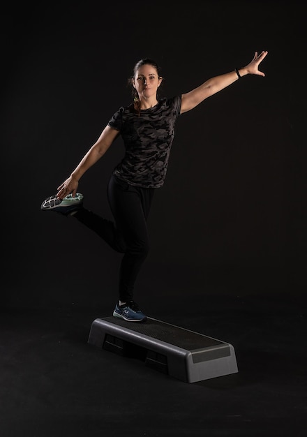 Mulher fitness na plataforma de passos fazendo exercícios Pratique esportes em um fundo preto Feliz