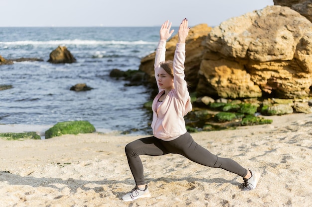 Mulher fitness praticando ioga asana poses na praia selvagem Warrior 1