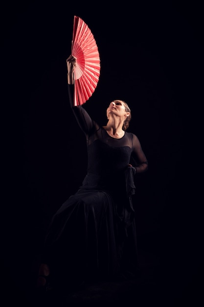 Mulher flamenca com vestido preto e leque vermelho olhando para cima