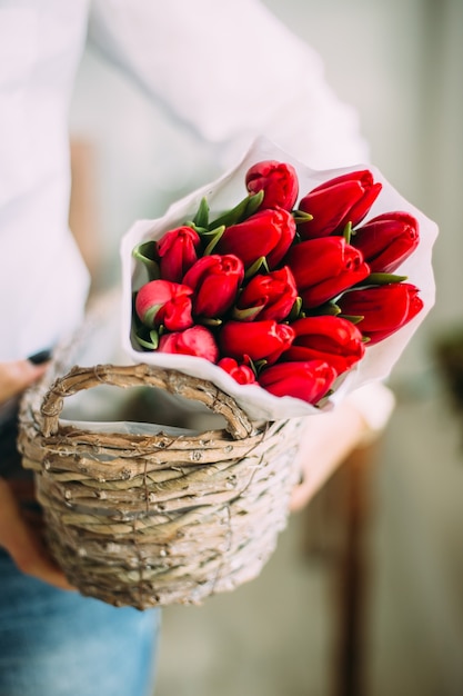 Mulher florista segurando uma cesta com tulipas vermelhas em papel branco. conceito de entrega de loja de flores