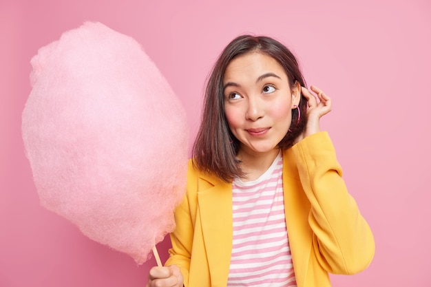 Mulher focada com uma expressão pensativa segurando um delicioso algodão doce no palito e usando roupas da moda