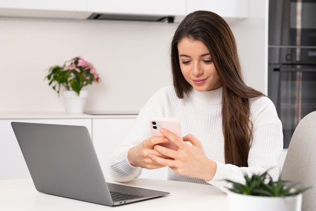 Mulher focada digita mensagem para namorado em smartphone senhora morena sentada perto de notebook e usa