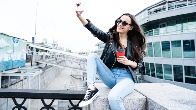 Mulher fofa e moderna tirando selfie em seu smartphone ao ar livre