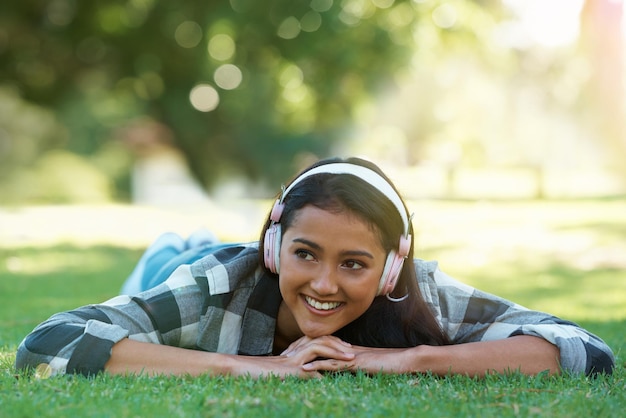 Mulher fones de ouvido e streaming de música em rádio de grama e internet para podcast ao ar livre Mulher feliz e relaxante na playlist de fim de semana de gramado e assinatura de áudio ou som em férias