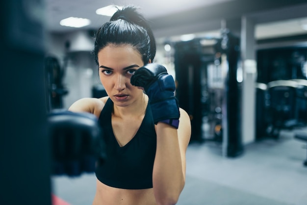 Mulher forte atleta morena atraente socando um saco com luvas pretas de kickboxing no treino de ginástica Estilo de vida e pessoas fitness esporte