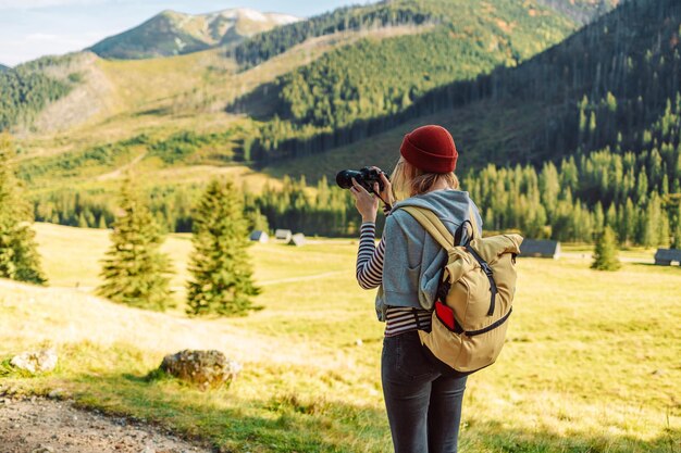 Mulher fotógrafa com mochila amarela está tirando uma foto da paisagem de outono nas montanhas tatras