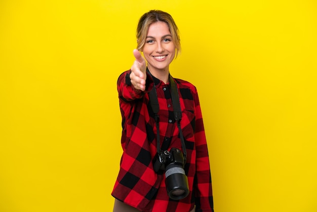 Mulher fotógrafa uruguaia isolada em fundo amarelo apertando as mãos para fechar um bom negócio