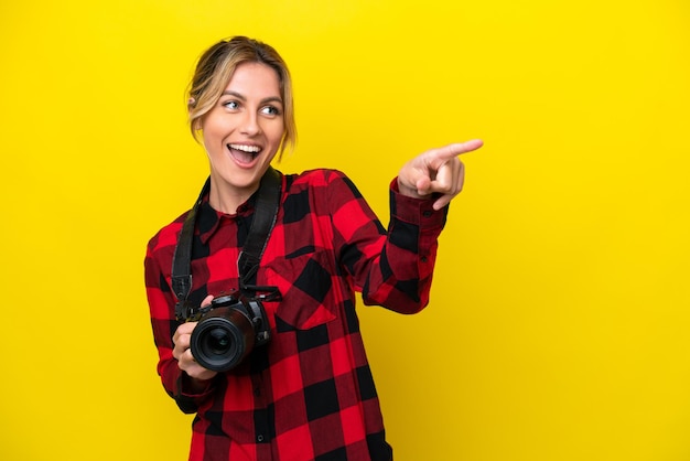 Mulher fotógrafa uruguaia isolada em fundo amarelo, apontando o dedo para o lado e apresentando um produto