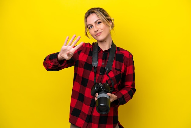 Mulher fotógrafa uruguaia isolada em fundo amarelo feliz e contando quatro com os dedos