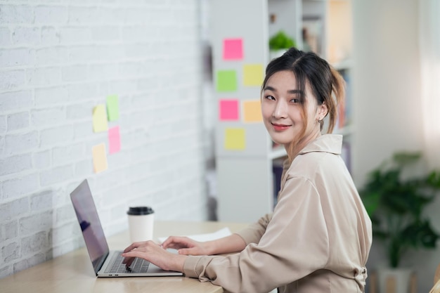 Mulher freelance asiática digitando no teclado e trabalhando no laptop na mesa de madeira em casa mulher empreendedora trabalhando para seu negócio na sala de estar em casa conceito de trabalho em casa de negócios