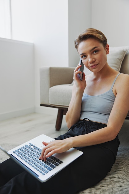 Mulher freelance com laptop e telefone trabalha em casa sentada no chão com suas roupas de casa com um corte de cabelo curto espaço de cópia gratuita