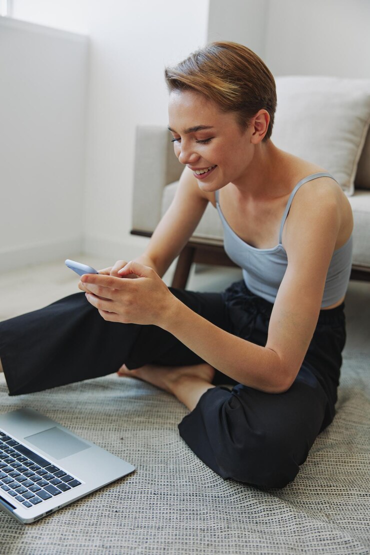 Foto mulher freelance com laptop e telefone trabalha em casa sentada no chão com suas roupas de casa com um corte de cabelo curto espaço de cópia gratuita