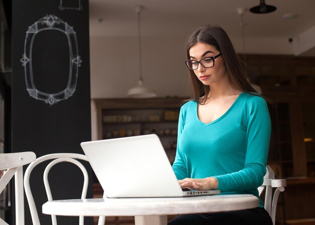 Mulher freelancer com óculos está trabalhando com seu laptop na mesa