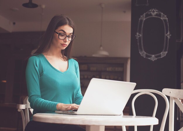 Mulher-freelancer com óculos está trabalhando com seu laptop na mesa