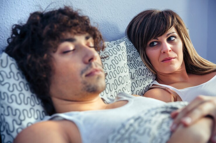 Foto mulher frustrada e com raiva, olhando para o jovem dormindo na cama. conceito de relacionamento e problemas de casal.