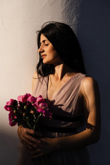 Foto mulher georgiana atraente com buquê de flores de peônias está posando na cidade ao pôr do sol modelo atraente em vestido de moda com flores estilo de vida