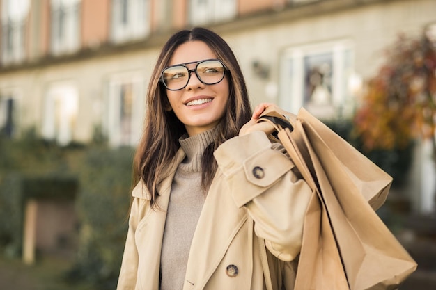 Mulher glamorosa em óculos da moda com sacolas de compras e lindo sorriso na rua