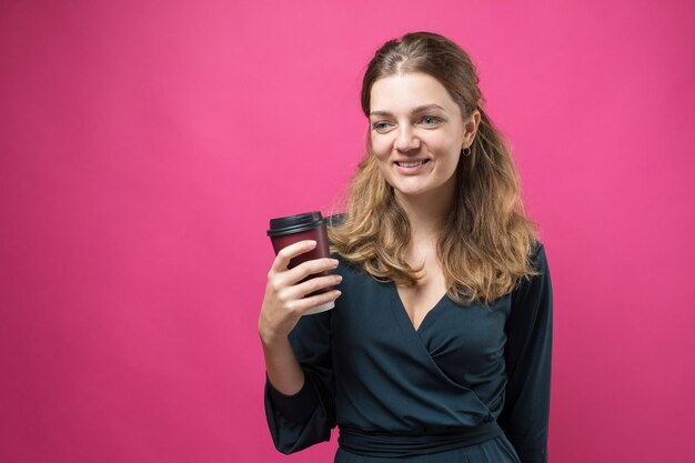 Mulher glamour em um vestido azul escuro com um copo de café em um fundo rosa