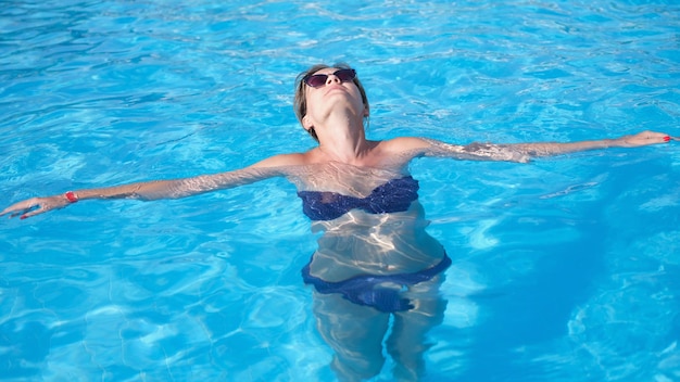 Mulher glamourosa em elegantes óculos de sol gosta de nadar em água turquesa na piscina