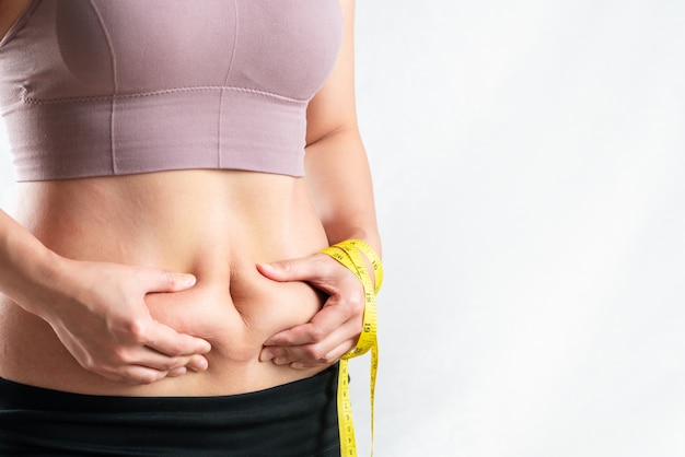 Foto mulher gorda, barriga gorda, gordinha, mulher obesa mão segurando excesso de gordura da barriga com fita métrica, conceito de estilo de vida de dieta de mulher