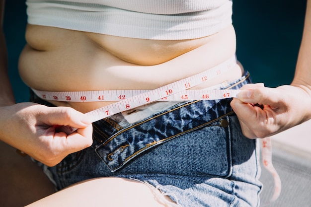 Mulher gorda barriga gorda mão de mulher obesa gordinha segurando gordura excessiva da barriga com fita métrica conceito de estilo de vida de dieta de mulher