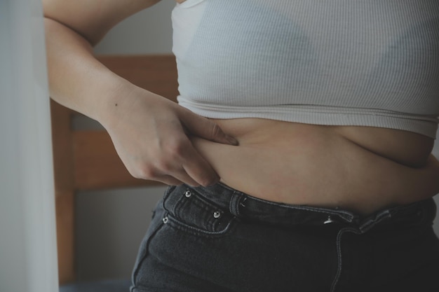 Mulher gorda barriga gorda mão de mulher obesa gordinha segurando gordura excessiva da barriga com fita métrica conceito de estilo de vida de dieta de mulher