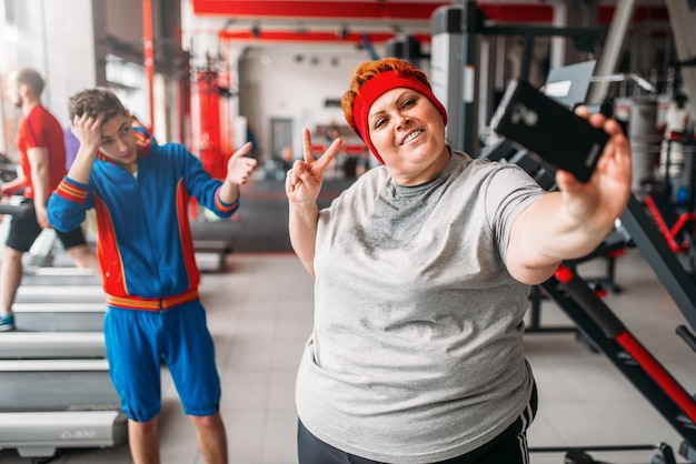 Mulher gorda faz selfie com instrutor de ginástica, humor. queima de calorias, mulher obesa em clube esportivo, queima de gordura
