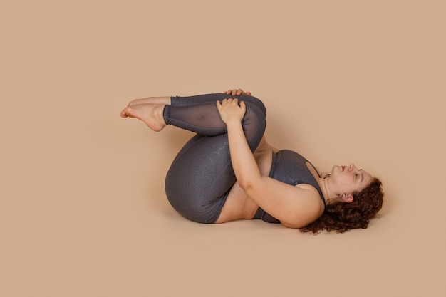 Mulher gorda ruiva com obesidade grande deitada de joelhos no peito pose asana yoga tentando perder peso Flex postura