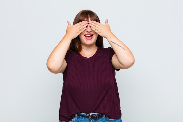 Mulher gorda sorrindo e se sentindo feliz, cobrindo os olhos com as duas mãos e esperando por uma surpresa incrível