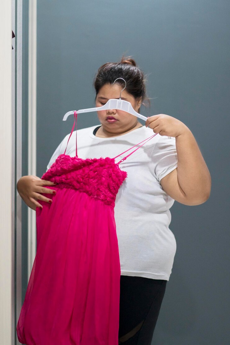 Foto mulher gorda tenta seu velho vestido com expressão triste