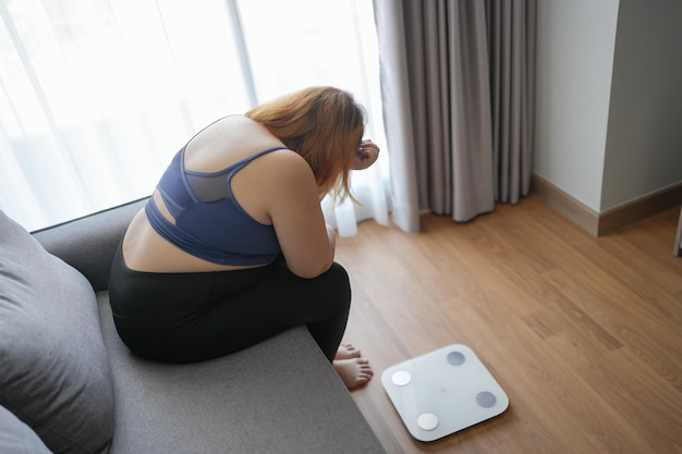 Mulher gorda triste com gordura chateada com a dieta Perda de peso falha Dieta gorda e escala triste Mulher asiática obesa na balança de peso em casa controle de peso