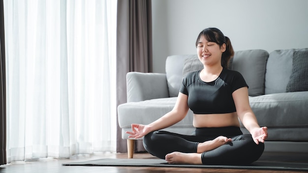 Mulher gordinha asiática sentada no chão na sala de estar pratica aula de ioga