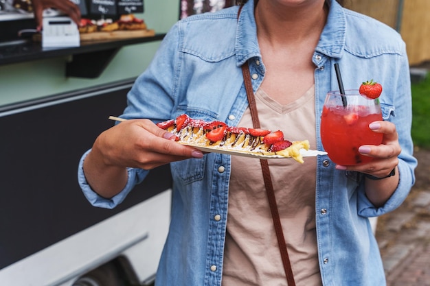 Mulher gosta de deliciosas panquecas com morangos e daiquiri de morango em um festival de comida Crepes com morangos frescos e chantilly comida de rua Food trucks food festival